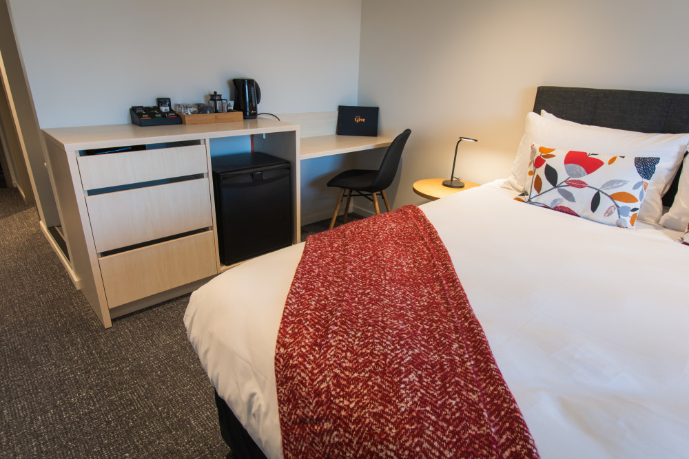A desk, bed and mini fridge in Hotel Give's Deluxe Queen room